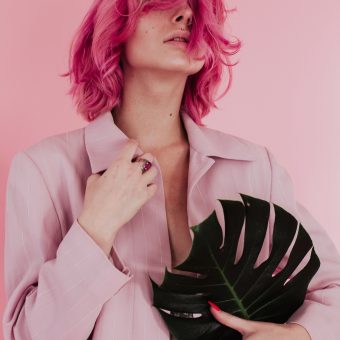 young-woman-with-dyed-hair-holding-leaf-while-standing-against-colored-background